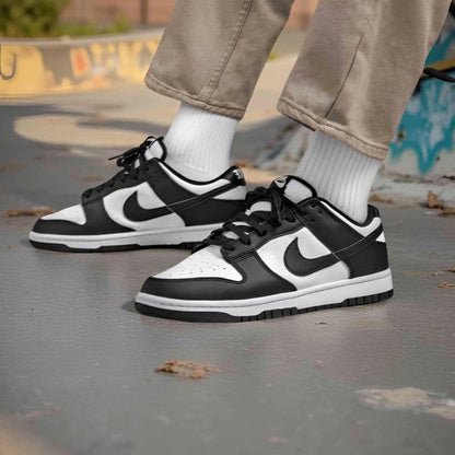 Black and white sneakers with a Nike logo worn on a concrete surface.